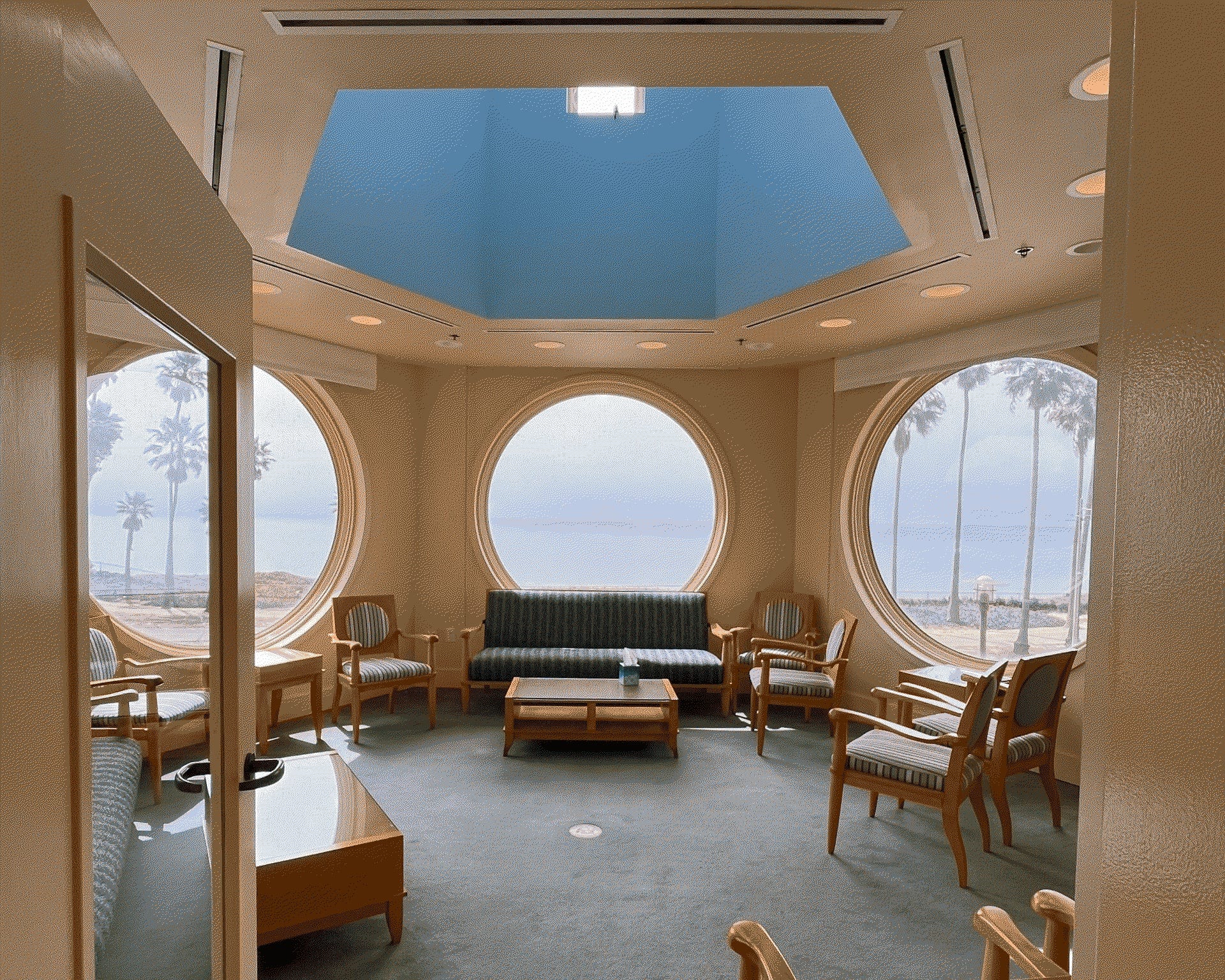Sunlit circular Tower Room meeting room in Kohn Hall with a blue skylight, round windows, a sofa, and striped wooden armchairs overlooking palm trees and the ocean.