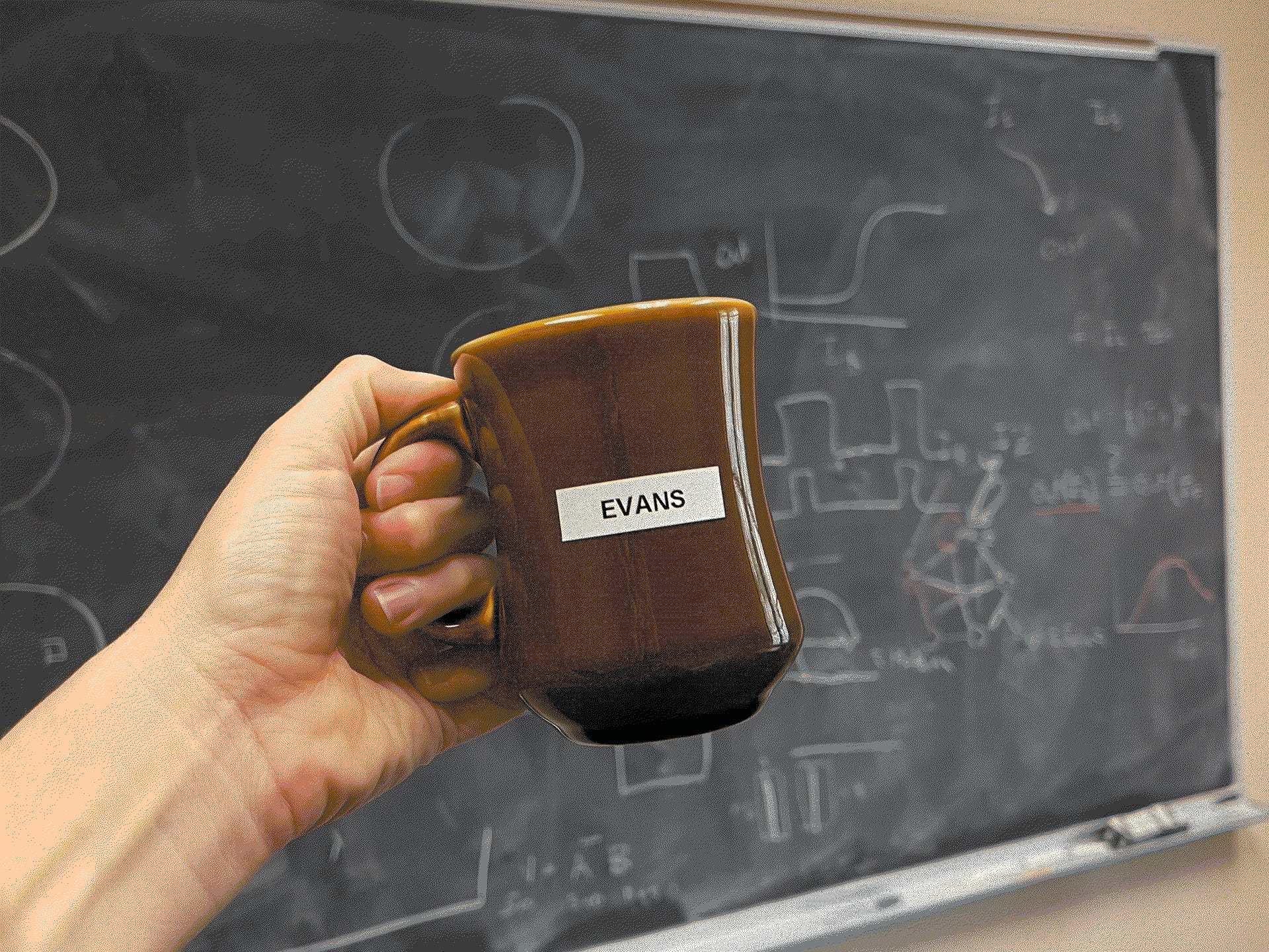 Hand holding a brown mug labeled “EVANS” in front of a chalkboard covered with mathematical markings.