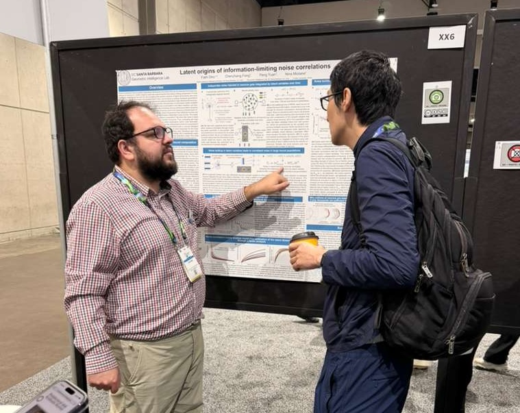 Two people discuss a scientific poster titled “Latent origins of information-limiting noise correlations” at an indoor conference.