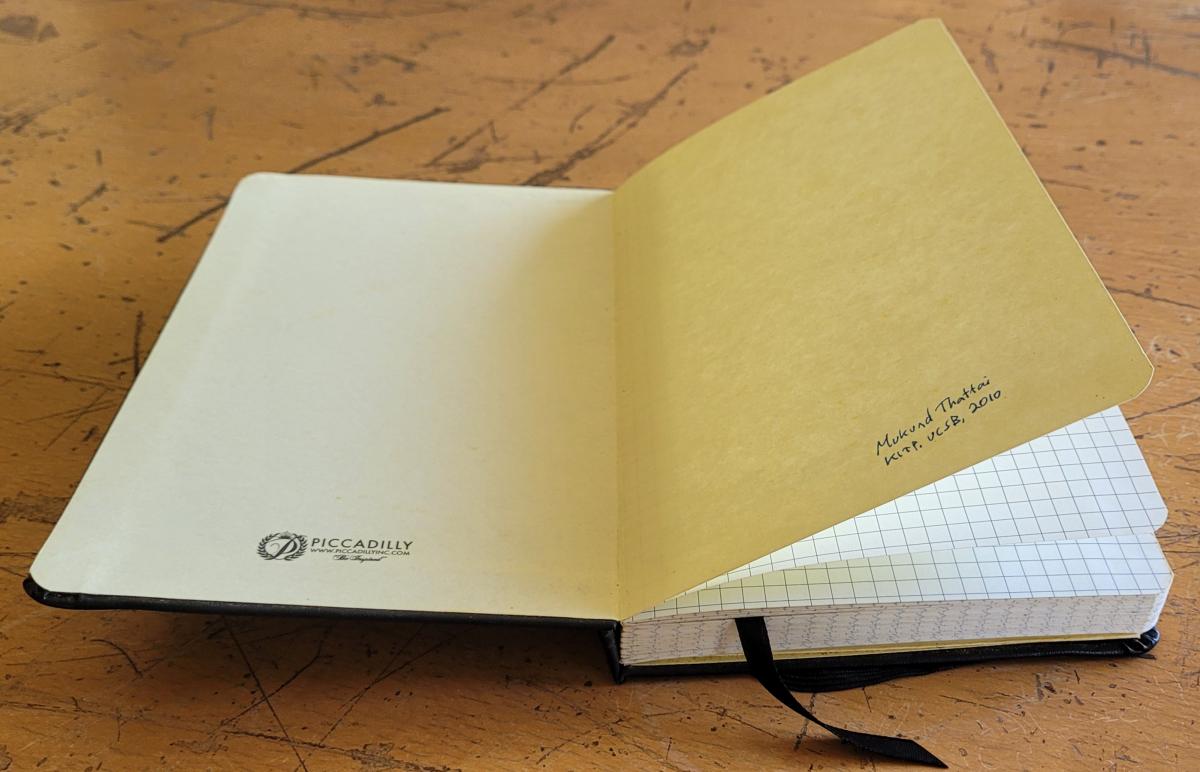 A notebook opened to the first page with a handwritten label 'Mukund Thattai, KITP, UCSB, 2010'