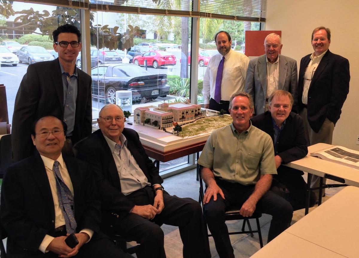Eight men seated and standing in front of an architectural model